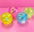Four colourful clear glitter apple squishies on a pink background